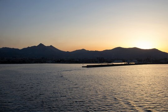 evocative image of the view of the city of Palermo from a ferry with the mountains in the background at sunset
