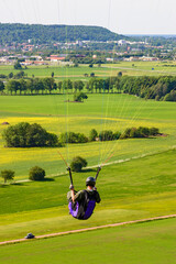 Paraglider sitting in a harness and flying over a rural landscape