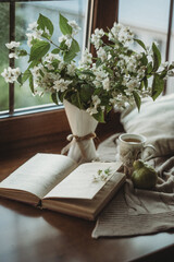 a spring bouquet of jasmine flowers stands on the window, a book lies next to it and there is a mug of tea