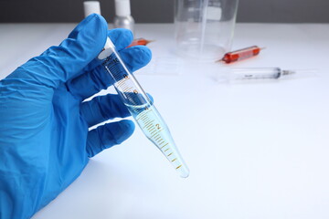 glass test tube is used by hands on the white table with syringe , beaker, and blood tubes which are testing for laboratory research the vaccine to protect the corona virus covid19 in lab test project