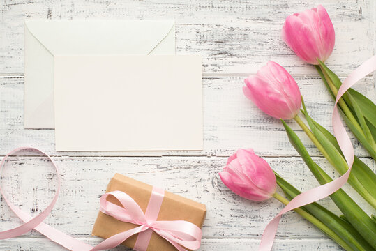 Happy women's day concept. Photo of bouquet of tulips wrapped giftbox and white blank empty card for text design on wooden white desk