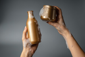 Young woman holds shower gel bottle in her hands. on a gray background. Shower gel in foam. Gold bottle mockup