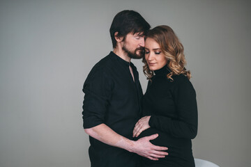 A happy man stands next to his pregnant girlfriend. loving parents are waiting for the birth of a baby. Husband hugs his pregnant wife's stomach