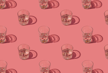 Gin and tonic crystal glasses garnished with rose buds and red peppercorns on a pastel pink background. Creative summer drink pattern.