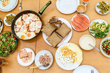 Healthy breakfast with family. Top view. Serving of eggs, bread, avocado, smoked salmon, cheese and salad from fresh vegetables on a wooden table,