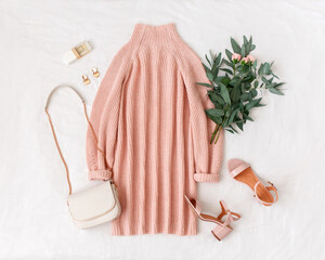 Pink knitted sweater dress, small bag with chain strap, heeled sandals, bouquet of flowers on white background. Women's stylish spring outfit. Trendy casual clothes. Flat lay, top view.