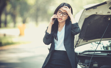 Asian business woman sad waiting for help by a broken car. Use a mobile phone to call the mechanic.