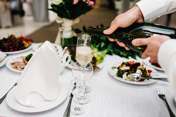 Man pours champagne in wineglasses. Bartender pouring champagne into glass, close-up.