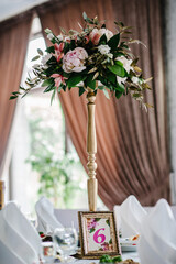A composition of flowers and green is on a festive table at the wedding banquet hall. Stands, sign number 6. Close up.