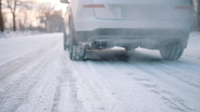 Frozen car driving on the road covered with snow leaving smoke behind. Close up on the wheel. High quality 4k footage