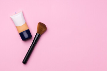 Bottle of liquid foundation and make up brush on pink background