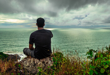 man sitting at mountain cliff enjoying the breathtaking view of sea horizon at morning