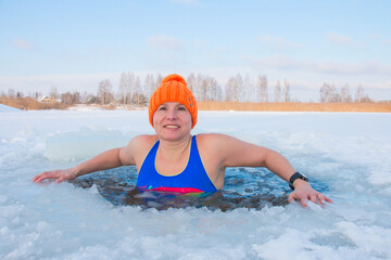 48 year old woman in an orange hat entered the ice hole in winter, extreme swimming at -15 frost