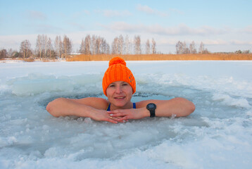 48-year-old woman in an orange hat bathes in an ice-hole in winter, extreme swimming at -25 frost
