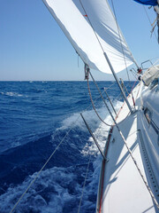 Aboard a sailboat yacht with main sail and genoa sailing fast heeling at a tipping angle on ocean sea.