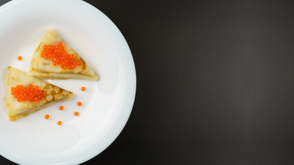 Pancakes with caviar. Thin pancakes, folded in triangles, lie on a white plate. Black background, with copy space