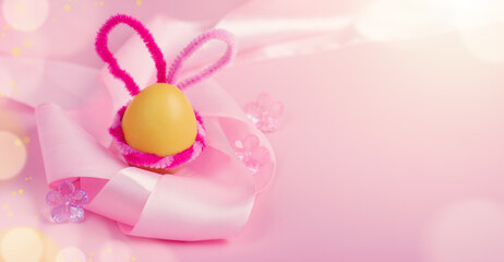 Banner with a yellow Easter egg with pink bunny ears and satin ribbon on a pink background. Easter card. Horizontal format, banner. Copyspace