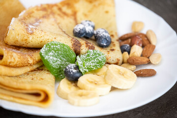 Pancakes with nuts, blueberries, banana and mint leaves. Close-up on a served plate with sweet dessert.