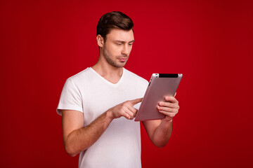 Portrait of half turned handsome young person using tablet look screen isolated on burgundy color background