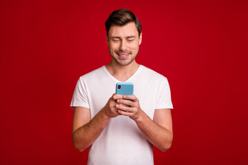 Photo portrait of young man using smartphone app typing message isolated bright red color background