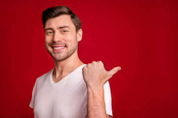 Photo of cheerful guy beaming smile indicate thumb empty space promotion isolated on dark red color background