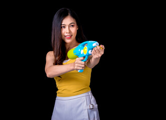 Portrait cheerful young asian woman Wearing a yellow tank top ,holding plastic water gun Smiling and having fun playing in the water Songkran festival, Songkran Thailand. isolated on black background.