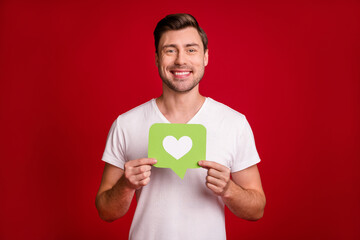 Photo portrait of happy guy showing like green card with heart smiling isolated vivid red color background