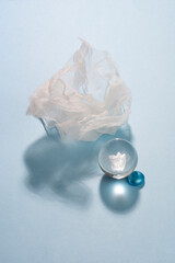 Glass ball, piece of white organza textile and blue pebble on blue background