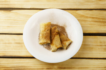 On a white plate, three pancakes sprinkled with cocoa, on a wooden background