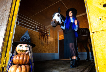 A girl dressed as a witch comes out of the corral with a horse, in the foreground an evil figure of...