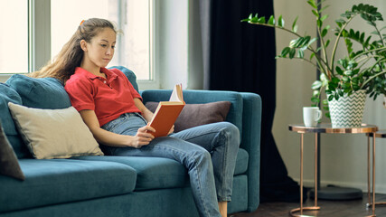 Obraz premium middle aged woman writing in notebook on sofa at home. beautiful woman at home writing and working with diary. Girl at home.