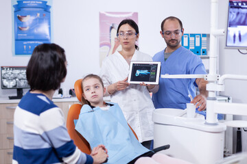 Obraz premium Pediatric dentist with tooth little girl digital radiography on tablet pc. Stomatologist explaining teeth diagnosis to mother of child in health clinic holding x-ray.