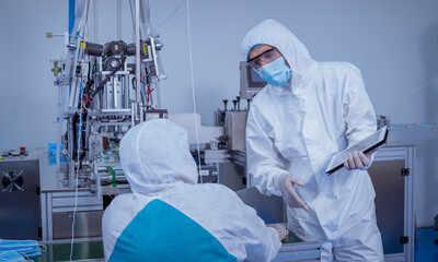 Technician worker wearing protective suite , glove are inspect ion with check  face mask manufacturing process to safe and against from virus. 