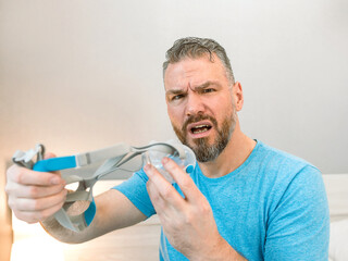 Unhappy shocked man with chronic breathing issues surprised by using  CPAP machine sitting on the...