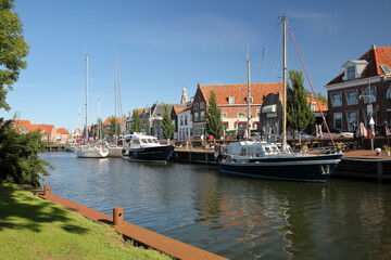 Fototapeta na wymiar Historic houses in Enkhuizen, West Friesland, Netherlands, with mooring sailing boats and the tower of Zuiderkerk (or St Pancraskerk) in the background
