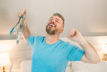 Happy rested man with chronic breathing issues after using  CPAP machine sitting on the bed in...