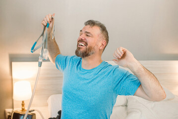 Happy rested man with chronic breathing issues after using  CPAP machine sitting on the bed in...