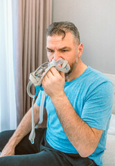 Unhappy shocked man with chronic breathing issues surprised by using  CPAP machine sitting on the...