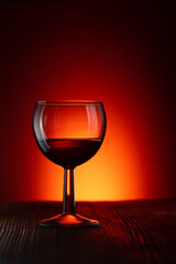 A glass of red wine stands on a wooden table against a dark illuminated background. Vertical banner