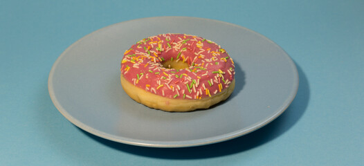 Pink doughnut or donut with colored sprinkles on a blue background. Bitten off American bagel.