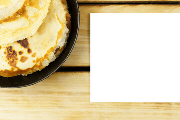 White sheet of paper next to a stack of pancakes on a wooden background.