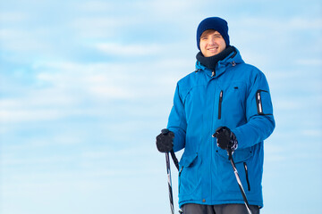 Close-up portrait. Happy young guy holding cross-country skis and sticks in his hands. The man...