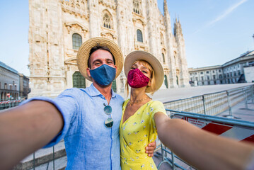 Friends wearing protective face mask taking a selfie in front of Duomo cathedral, Milan - Couple traveling Italy during Coronavirus pandemic period