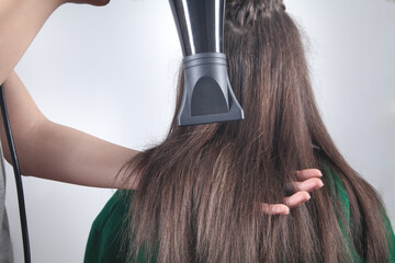 Girl drying hair with hairdryer in home.