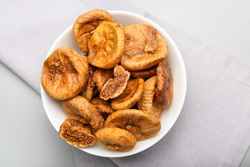 Bowl with tasty dried figs on light background
