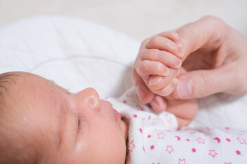 Little hand of a cute, adorable newborn girl holding the hand of her father