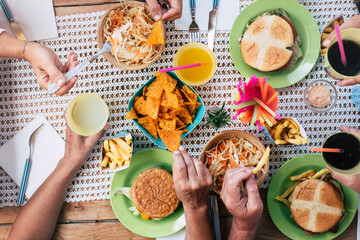 Close up of caucasian friends hands taking fast food hamburger and frech fries from the table - group of unrecognizable people eating and having fun together