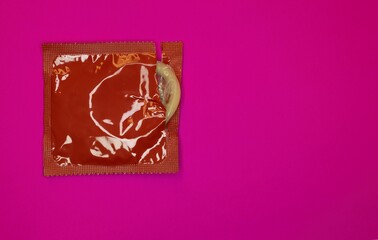 A partially open red condom on pink background
