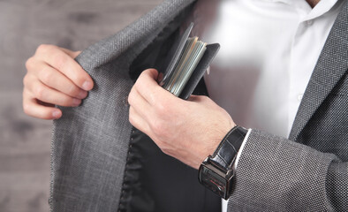 Businessman putting wallet with banknotes in suit pocket.