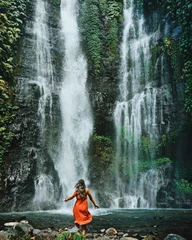 Fototapeten Bali Young woman standing in front of a very big and beautiful waterfall. Dancing next to sekumpul waterfall in bali, indonesia.   © Nadine